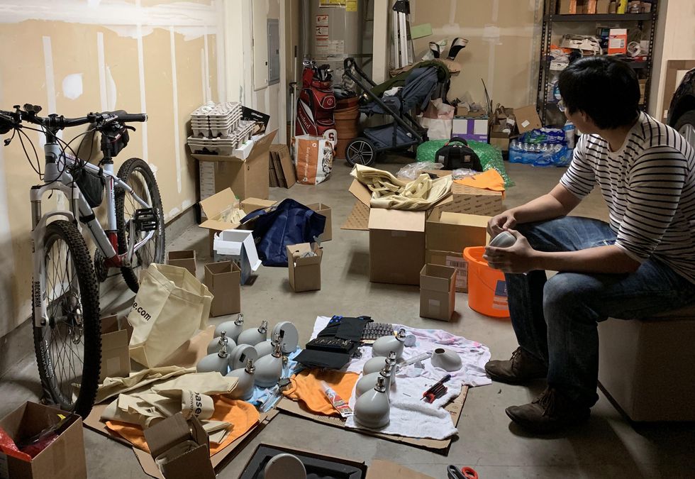 Man seated on box in garage with showerhead casings and parts laid out on the floor in front of him, he holds one showerhead.
